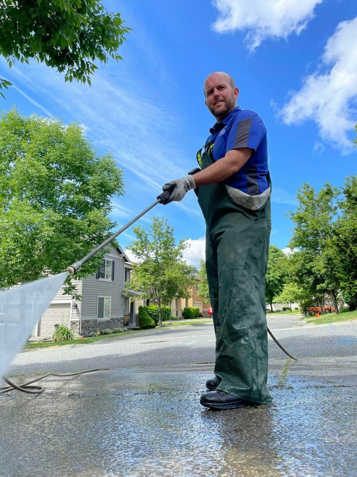 Man washing a driveway with a pressure hose, houses behind